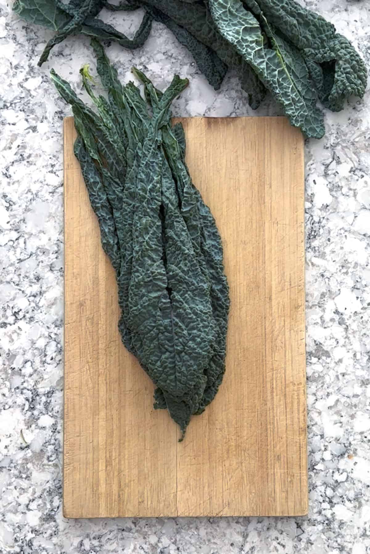 de-stemmed Tuscan kale leaves stacked up on a wooden cutting board.