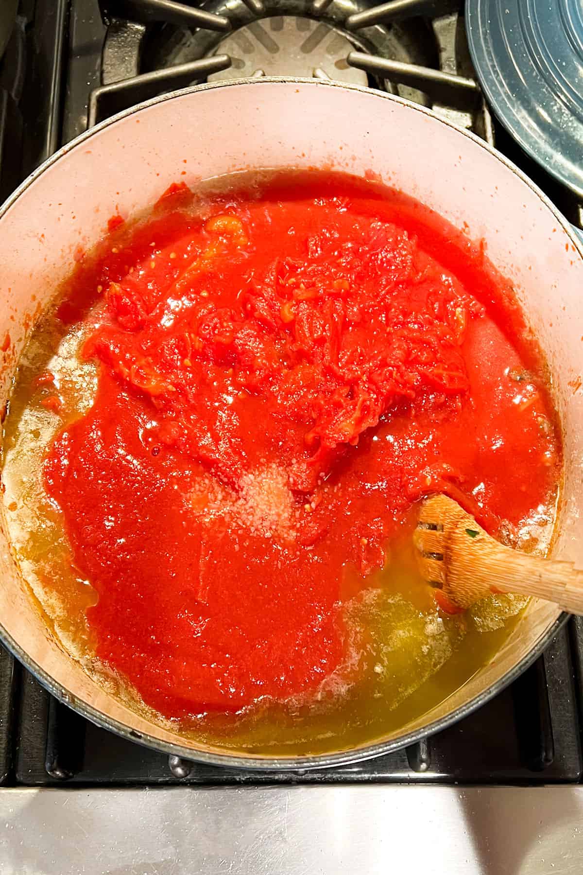 Crushed tomatoes being stirred into a sauce with a wooden spoon