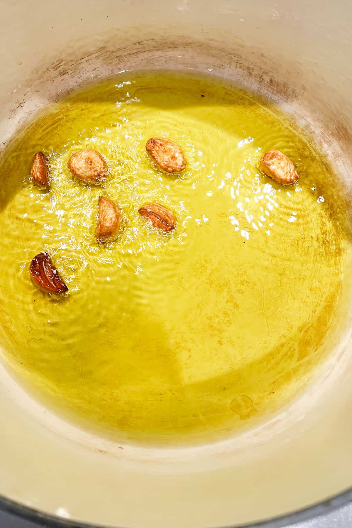 7 golden brown halved garlic cloves simmering in olive oil, in a Dutch oven.