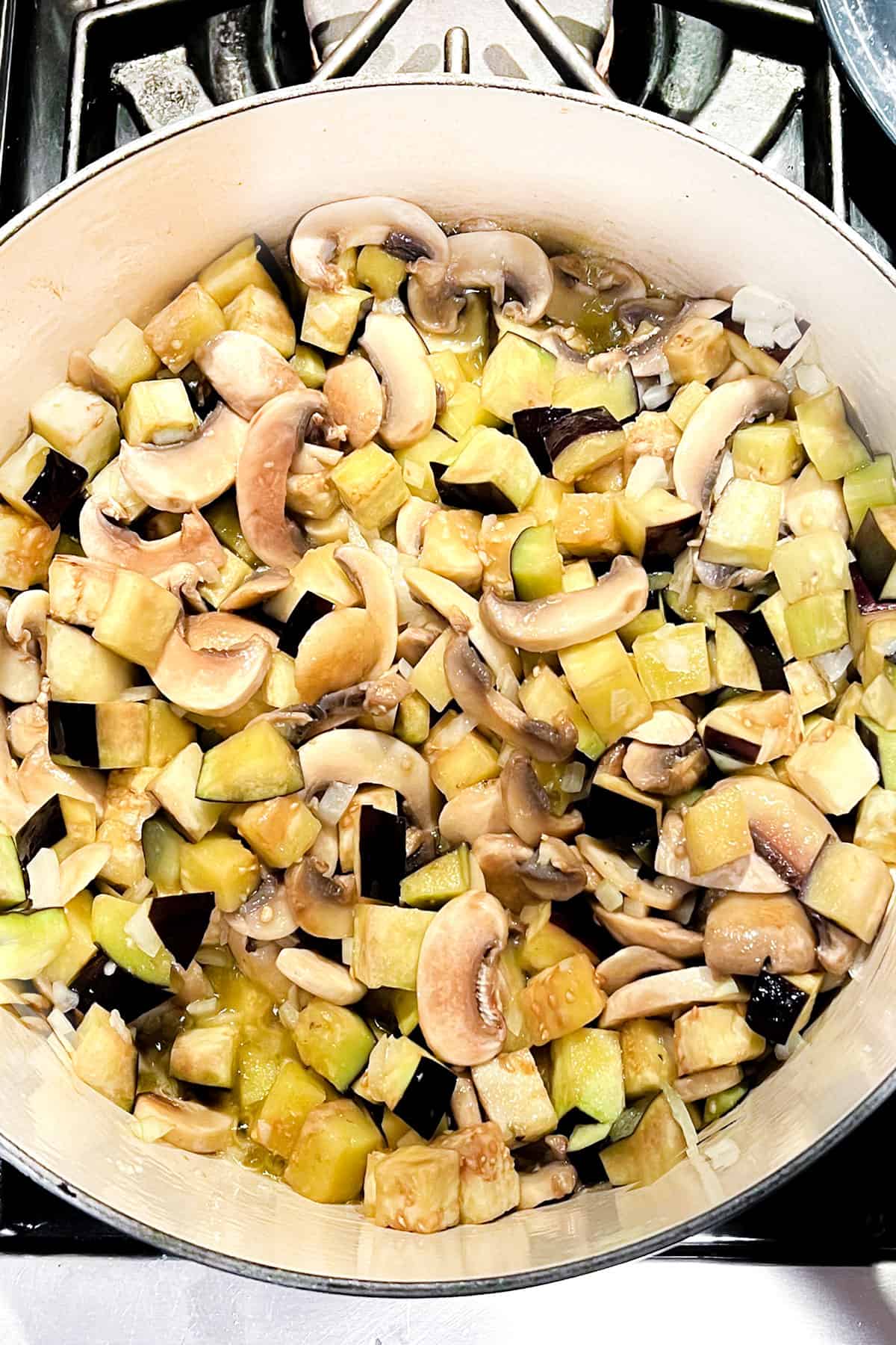 Sliced mushrooms, cubed eggplant and chopped onions simmering in a dutch oven.