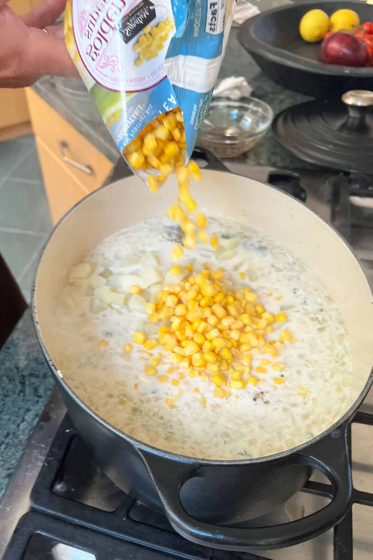 corn kernels being poured from a bag held above a dutch oven filled with shrimp chowder being cooked on the stove