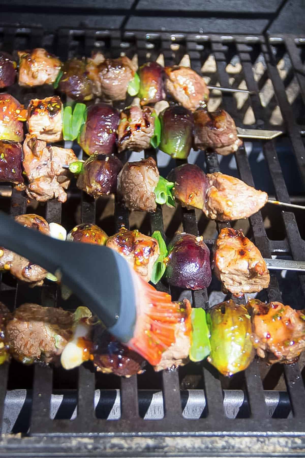 5 lamb and fig skewers on a grill rack being brushed with glaze