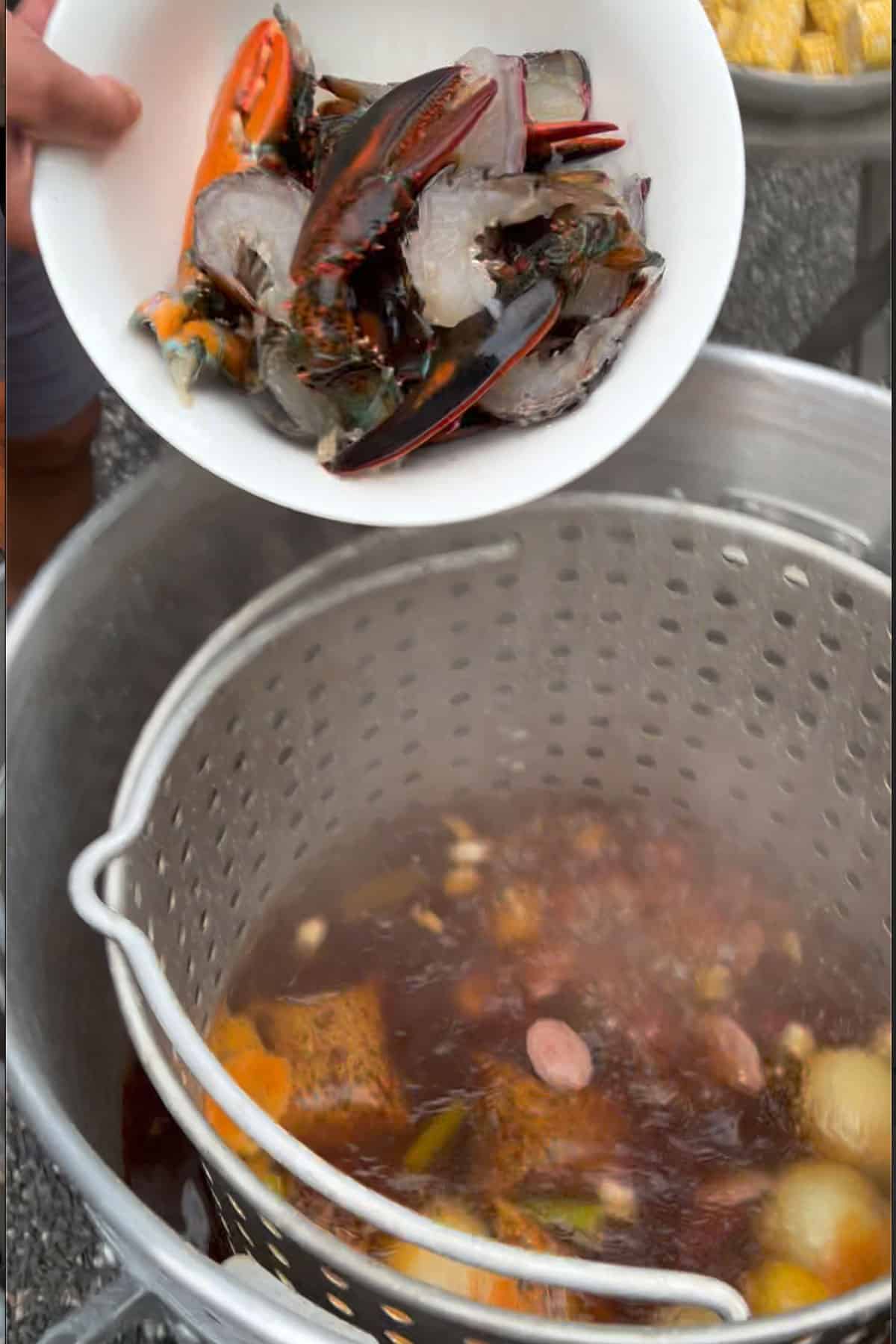 a bowl with raw lobster tails and claws getting poured into a seafood boilihng pot