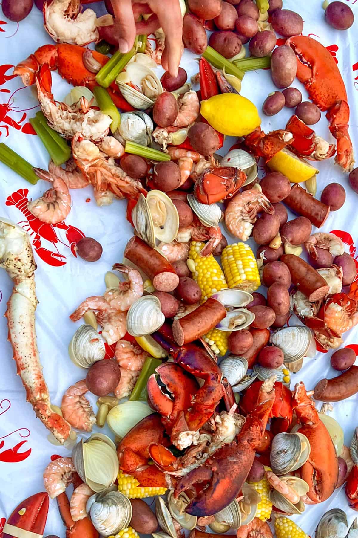 table covered with lobster claws, shrimp, crab legs, lemons, corn, celery shrimp and clams.