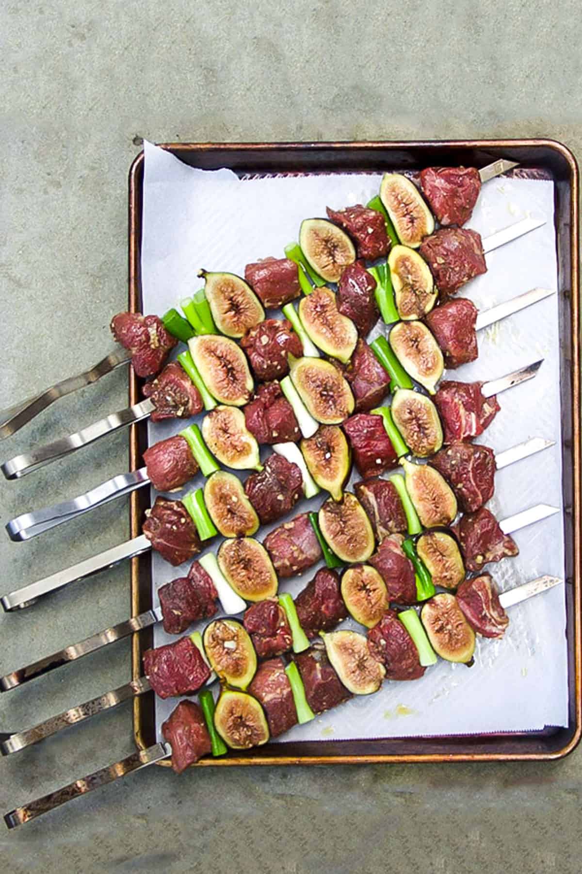 7 metal skewers threaded with cubes of raw lamb, fresh fig halves and scallions