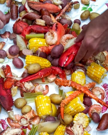 Hands reaching in to grab seafood from a table topped with a seafood boil