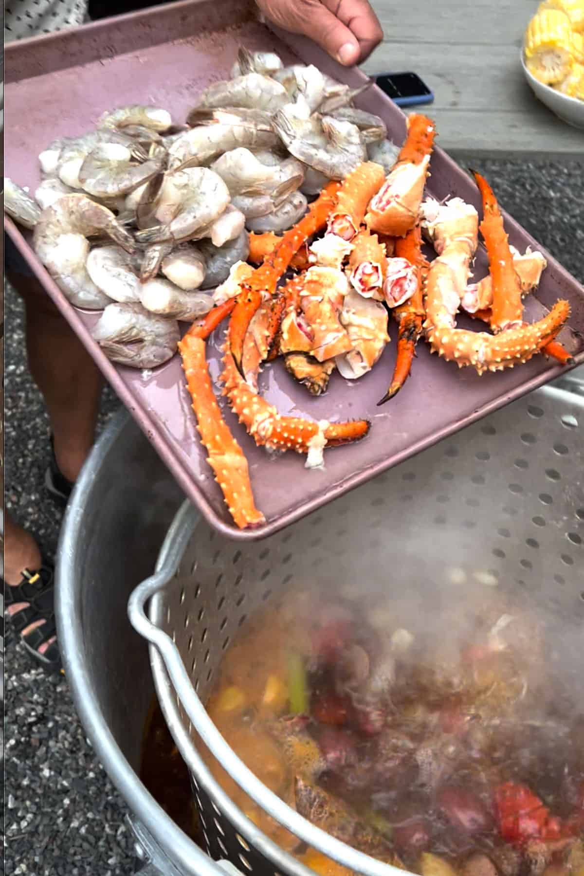 shrimp and king crab legs on a rimmed baking sheet getting poured into a pot of boiling seafood