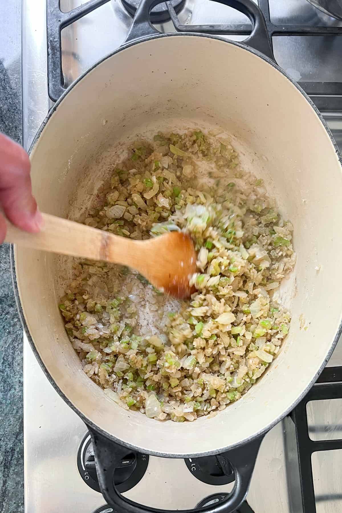 flour being stirred and cooked with sautéed onions, celery and garlic in a dutch oven.