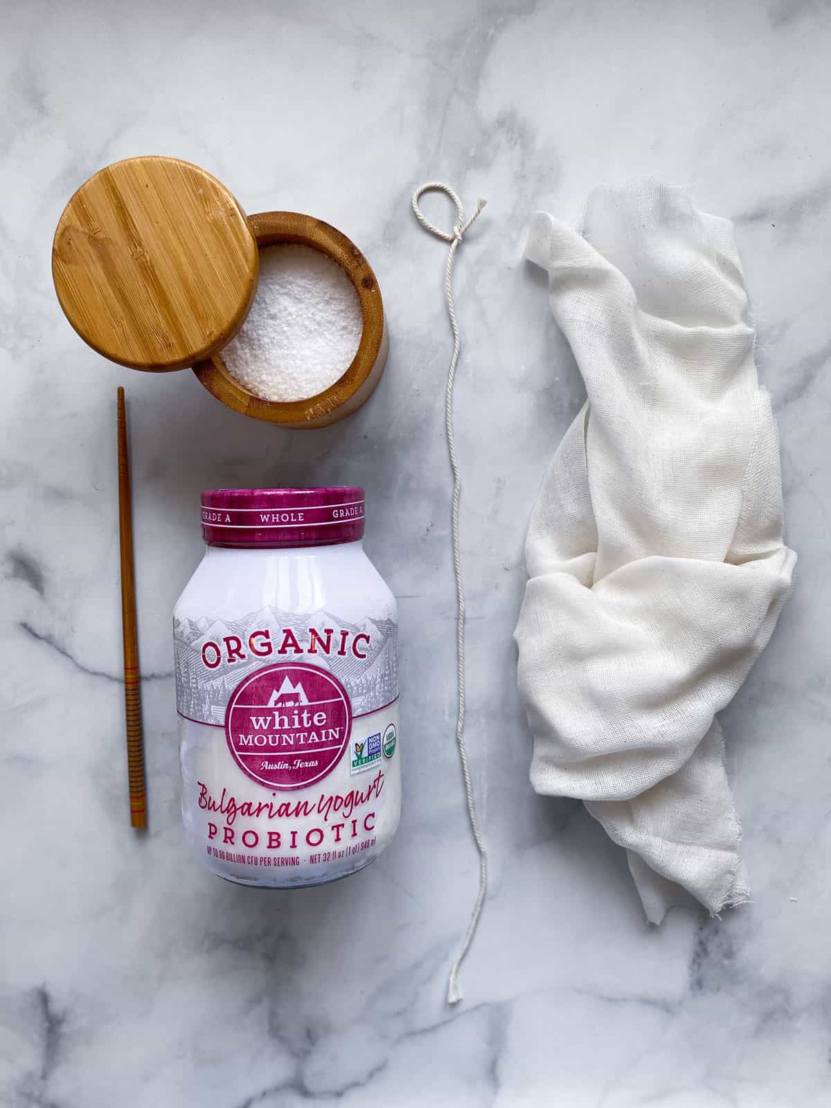 jar of bulgarian yogurt, bamboo tub of salt, cheese cloth, kitchen twine and a chopstick laying next to each other