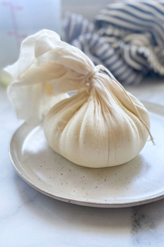 tied up cheesecloth full of labneh on plate