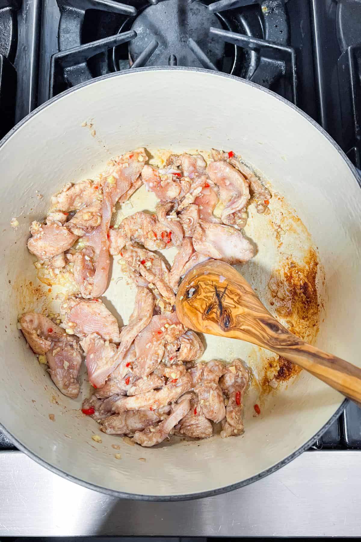 strips of marinated chicken cooking in a Dutch oven.