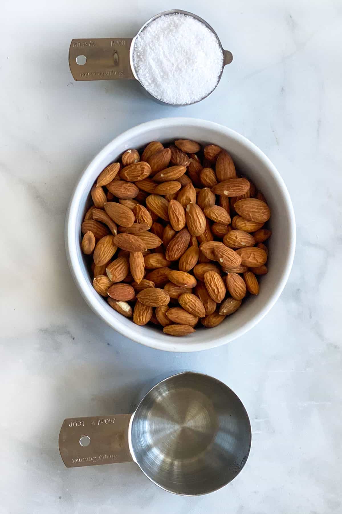 A measuring cup of salt, a bowl of almonds and a measuring cup of water