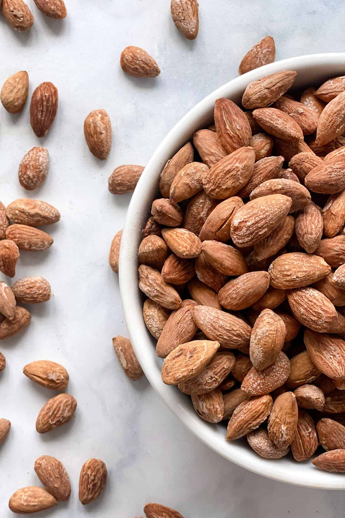 A bowl of salted almonds with salted almonds on a counter next to it