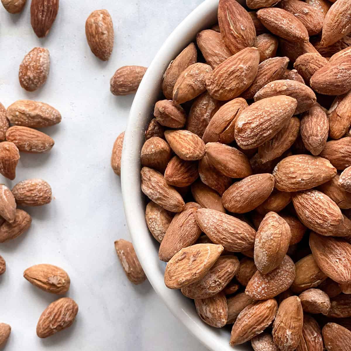 Roasted almonds in a bowl with roasted almonds scattered around