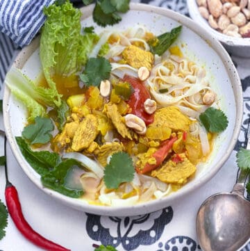 Bowl of noodles and chicken with herbs and lettuce topped with peanuts