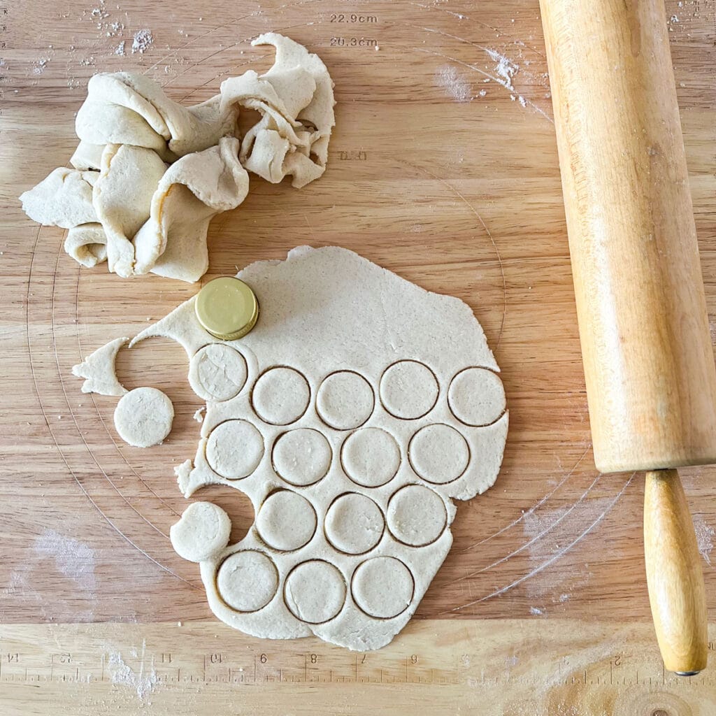 rolled out dough with circles punched in it from a bottle cap next to a rolling pin