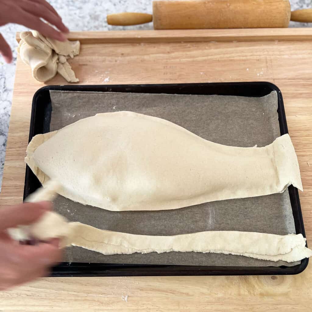 A whole red snapper wrapped in salt pastry that's been cut around the outline of the fish next to the excess pieces of dough
