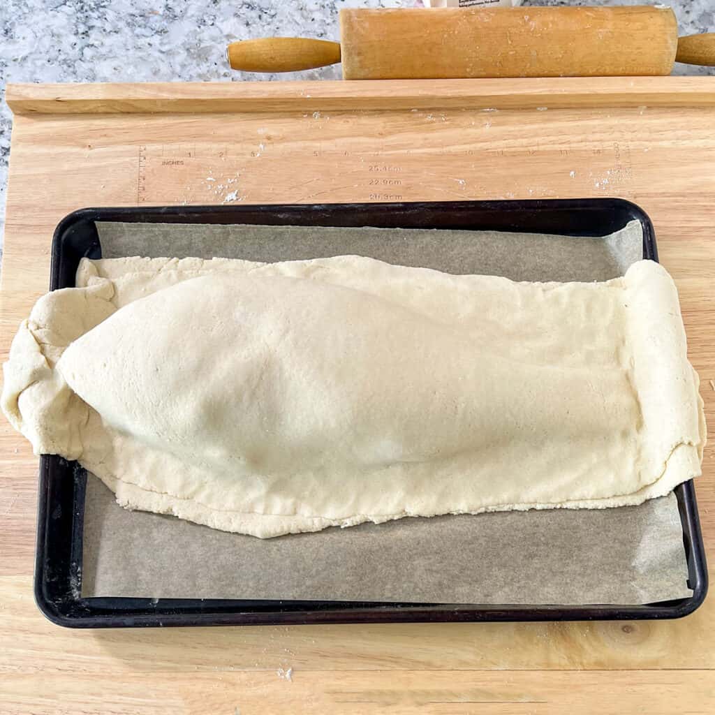 Salt pastry covering a whole red snapper on a parchment lined baking sheet