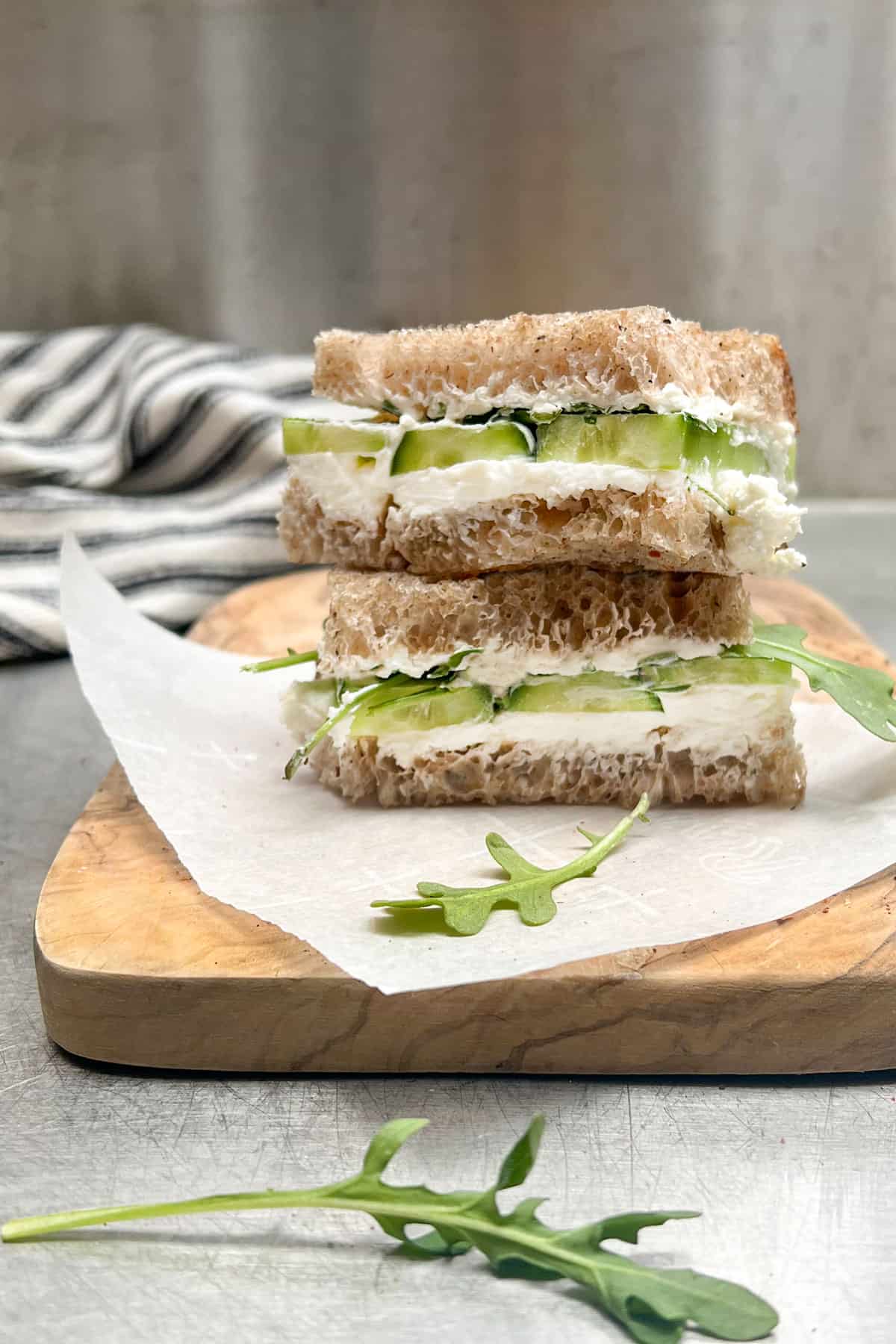 two halved of a cucumber labneh and arugula sandwich sitting on top of each other on a wooden cutting board