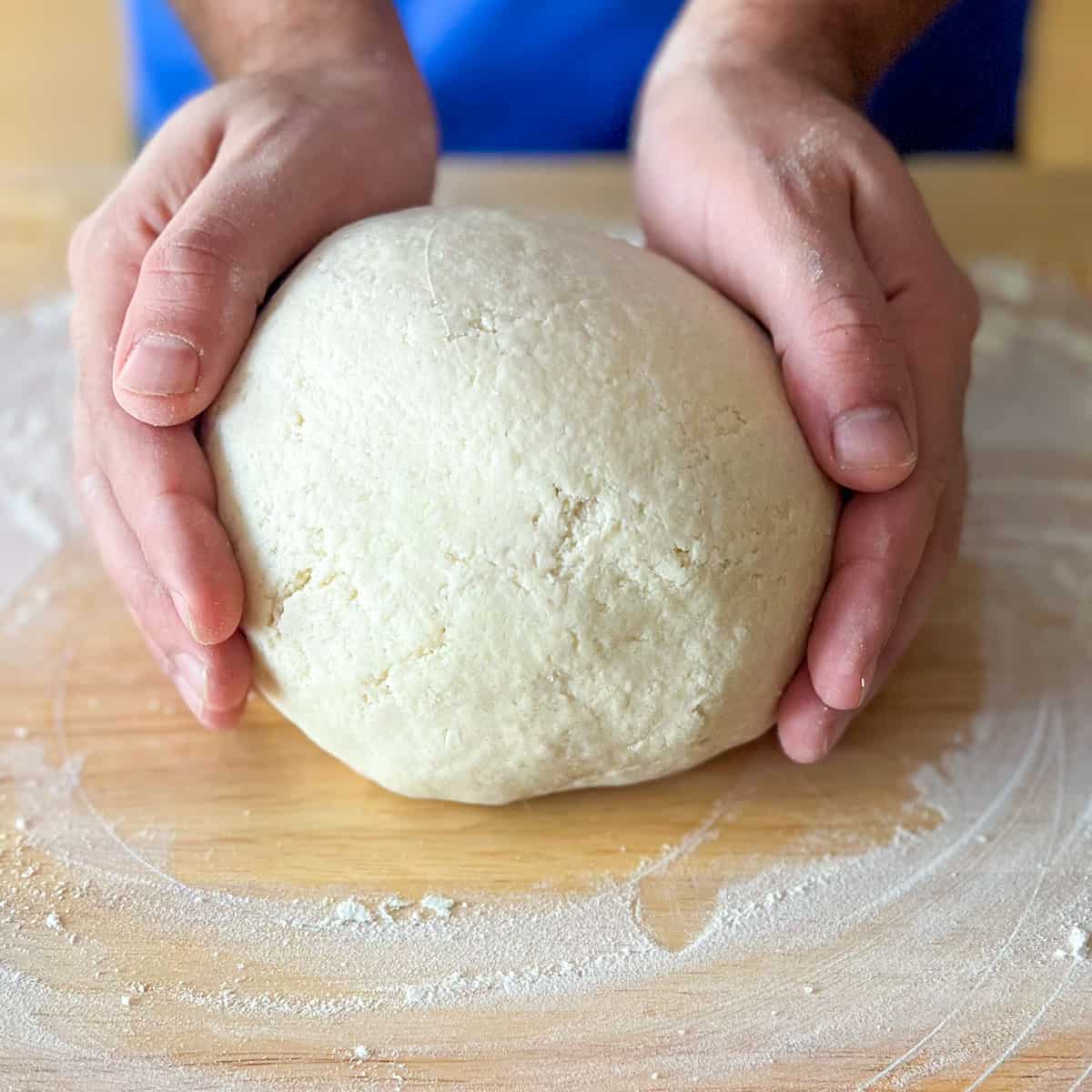 Two hands holding a ball of dough on a wooden cutting board