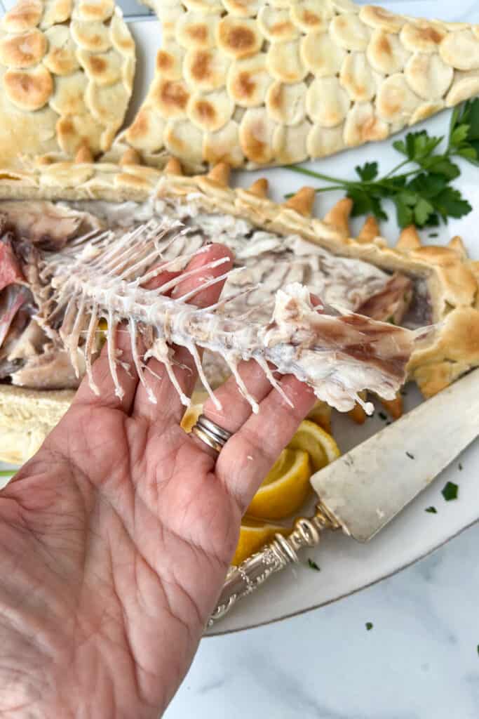 The spine being pulled out of a partially eaten whole red snapper with it's decorated salt crust in the background