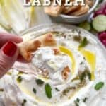 hand holding a piece of toasted pita slathered with labneh.