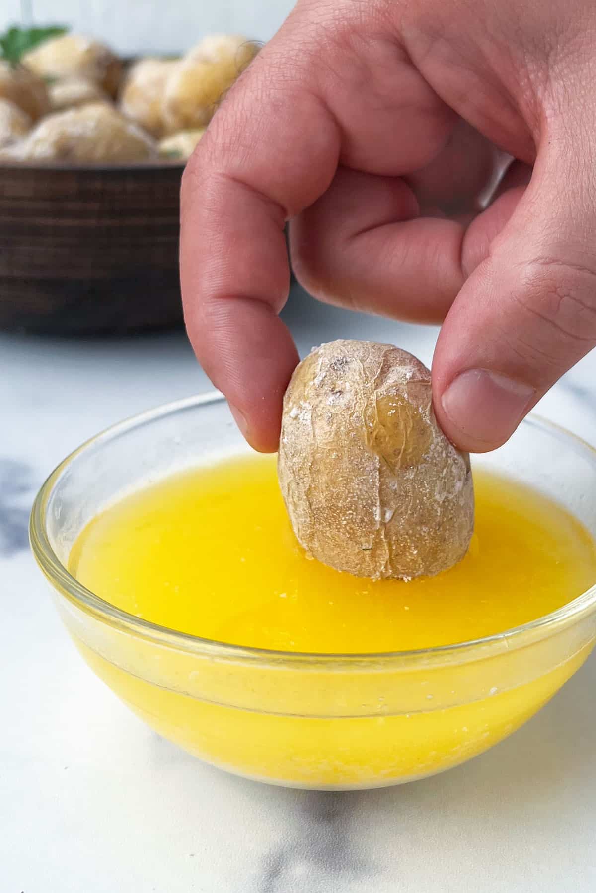 A hand holding a salt-crusted new potato and dipping it into a small glass bowl of melted butter.