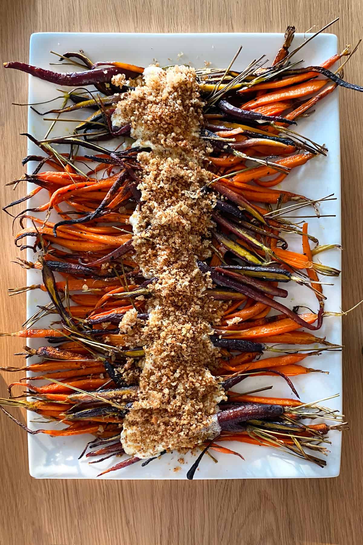roasted rainbow carrots on a platter topped with whipped feta and bread crumbs down the center.