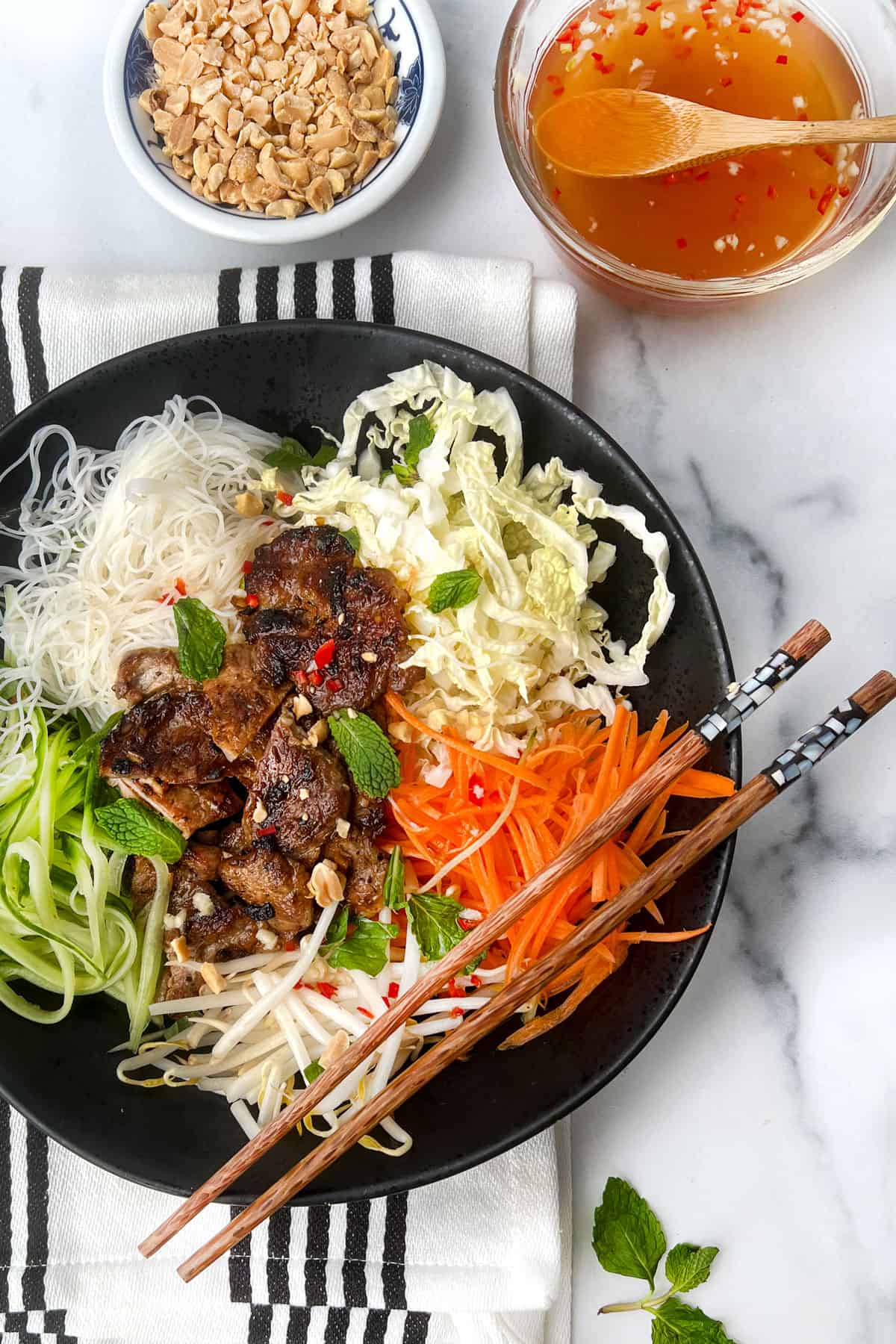 Vietnamese noodle salad bowl arranged with caramelized pork in the center and piles of shredded carrots, cucumbers and cabbage around it, along with a pile of vermicelli rice noodles and bean sprouts.