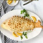 Salt pastry shaped like a fish with scales on top of a plate with lemons and parsley and a knife and fork in the background