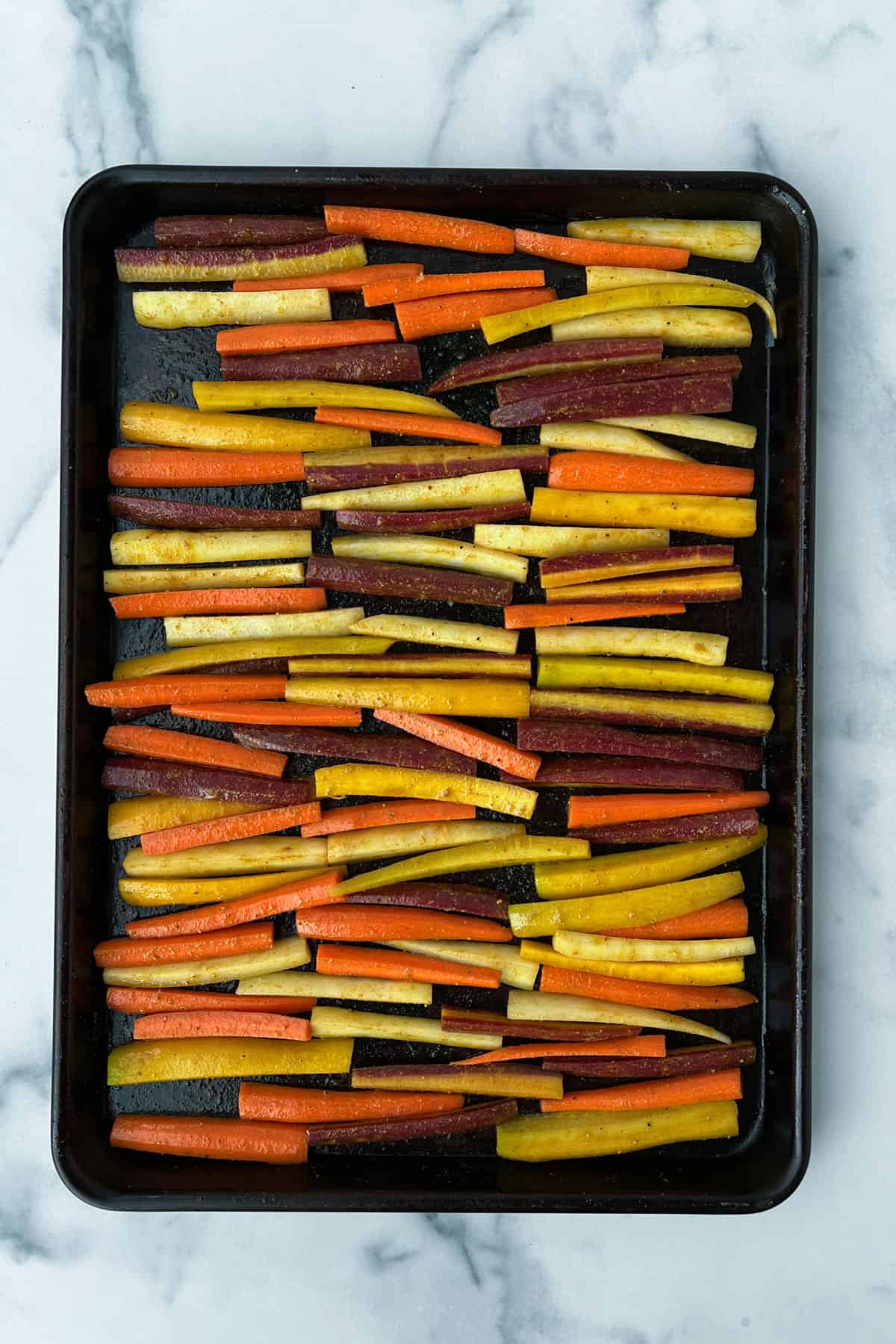 Rainbow carrot sticks arranged on a rimmed baking sheet.