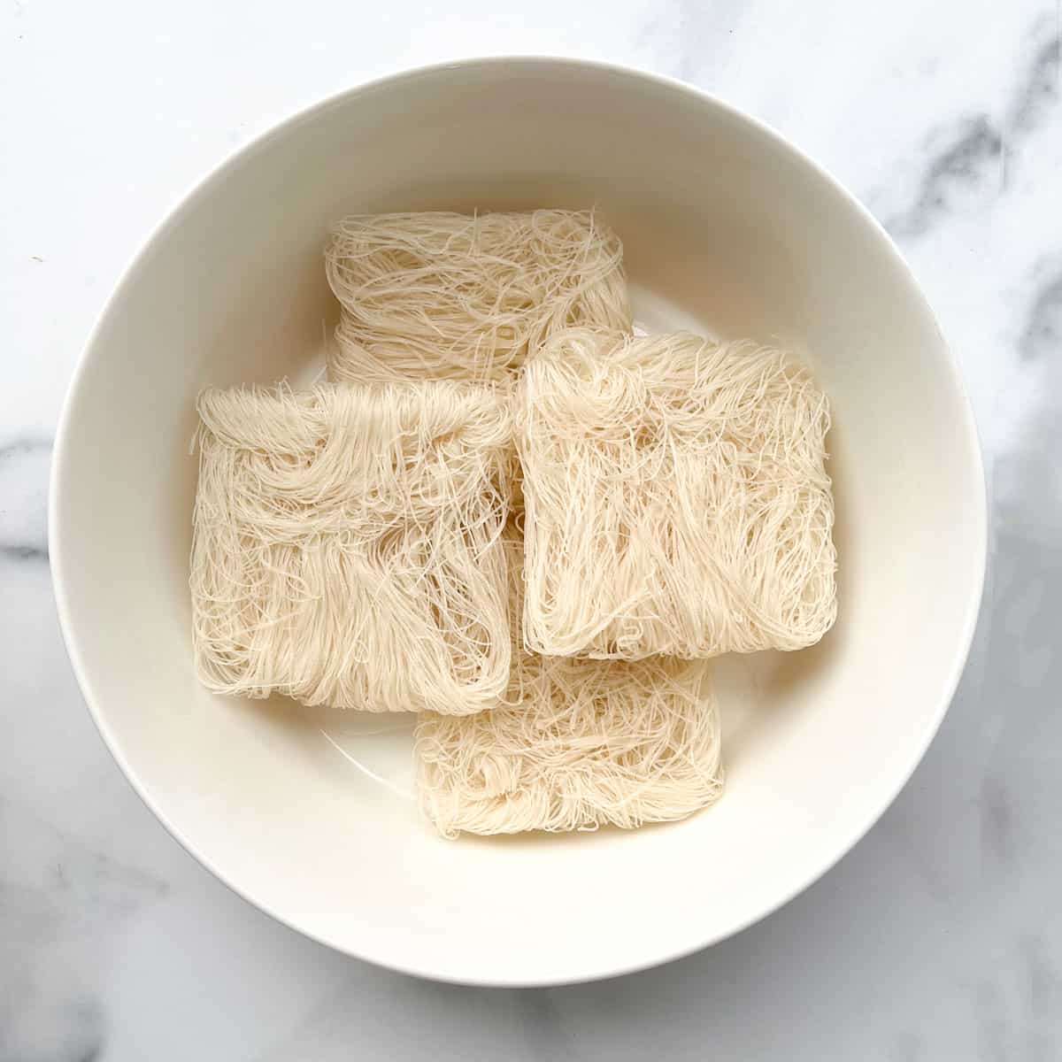 four bundles of dry rice noodles in a large bowl