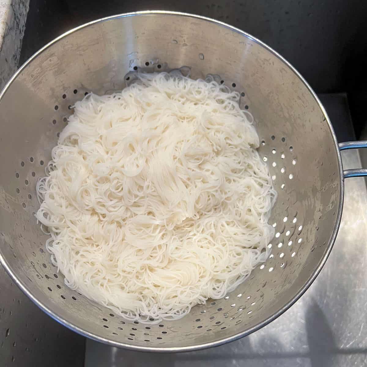 vermicelli rice noodles draining in a metal colander over the sink.