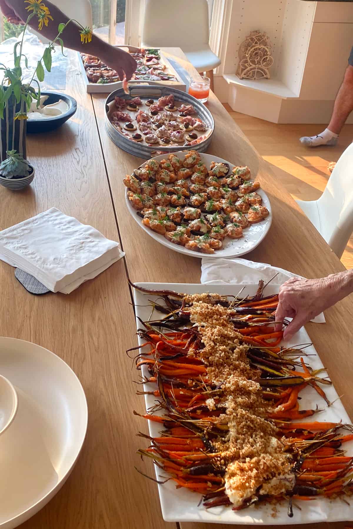 Table sset out with platters of appetizers including a large rectangular platter of roasted rainbow carrots with whipped feta down the center and toasted breadcrumbs sprinkled over the feta