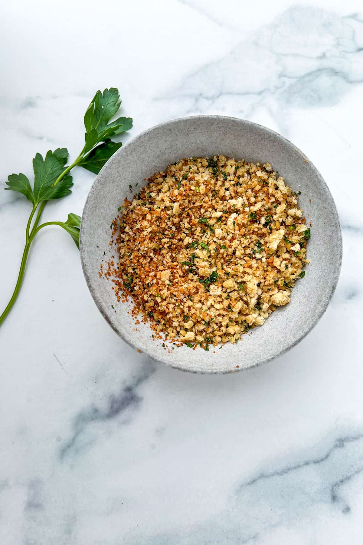 Toasted breadcrumbs mixed with parsley in a small wold on a marble counter.