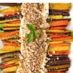 Two rows of roasted rainbow carrots arranged on a rectangular platter with whipped feta down the center and toasted bread crumbs sprinkled on top.