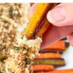 Hand holding one yellow roasted carrot with the tip covered in creamy whipped feta and toasted breadcrumbs.