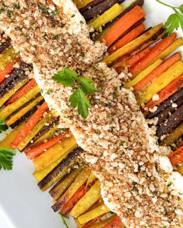 Two rows of roasted rainbow carrots arranged on a rectangular platter with whipped feta down the center and toasted bread crumbs sprinkled on top.