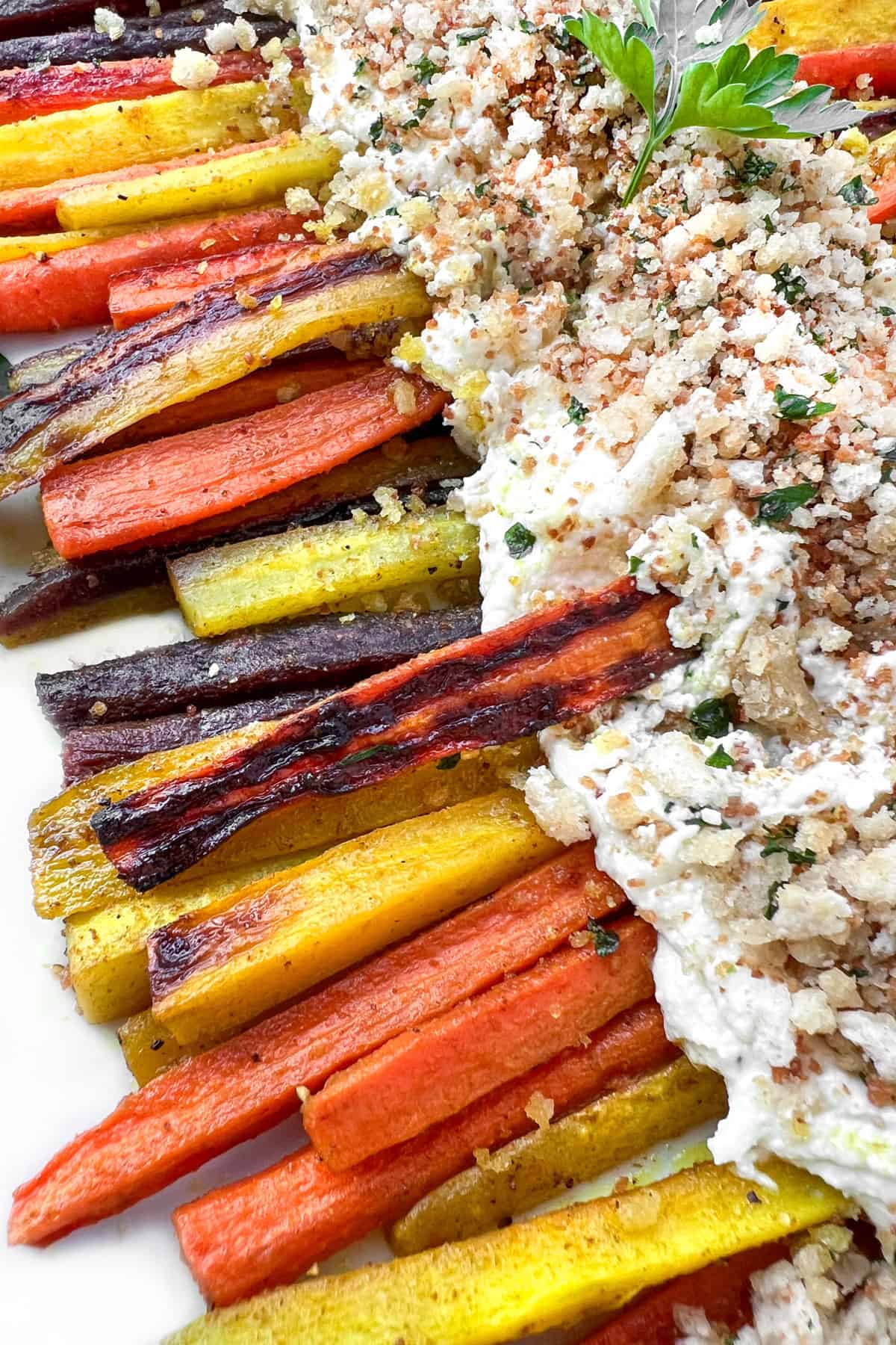 roasted rainbow carrot sticks arranged on a platter with creamy whipped feta topped with toasted breadcrumbs