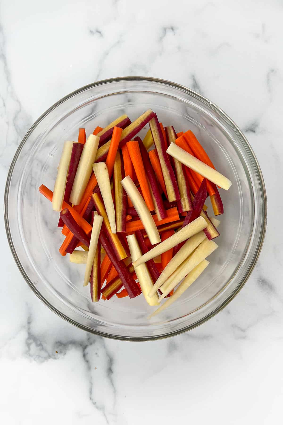 Rainbow carrot sticks in a glass mixing bowl