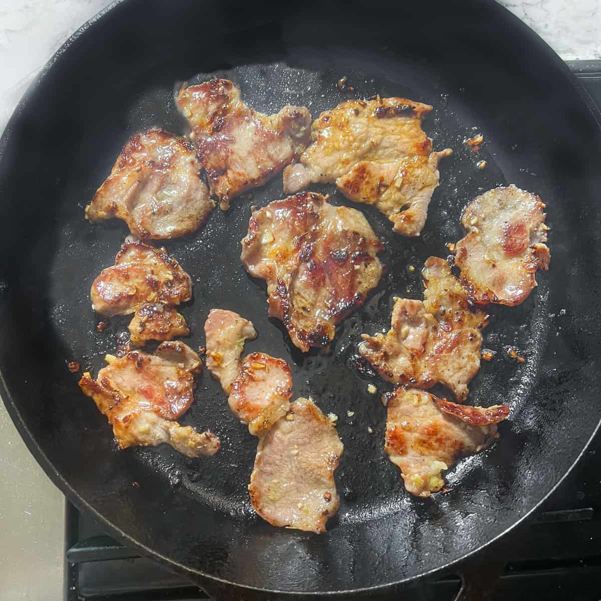 Pieces of marinated pork searing and caramelizing in a cast iron skillet