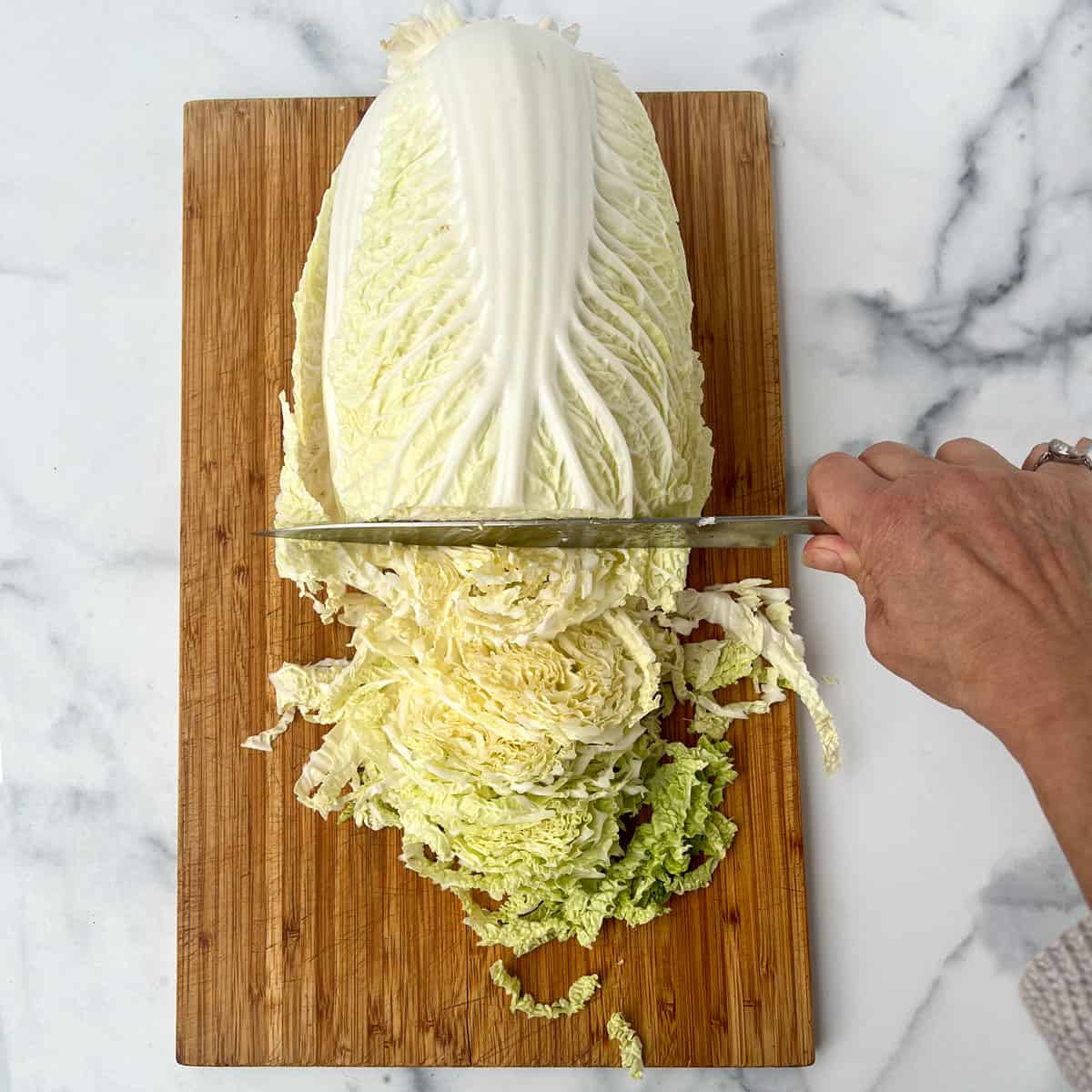 savoy cabbage on wooden cutting board being thinly sliced with a large knife.