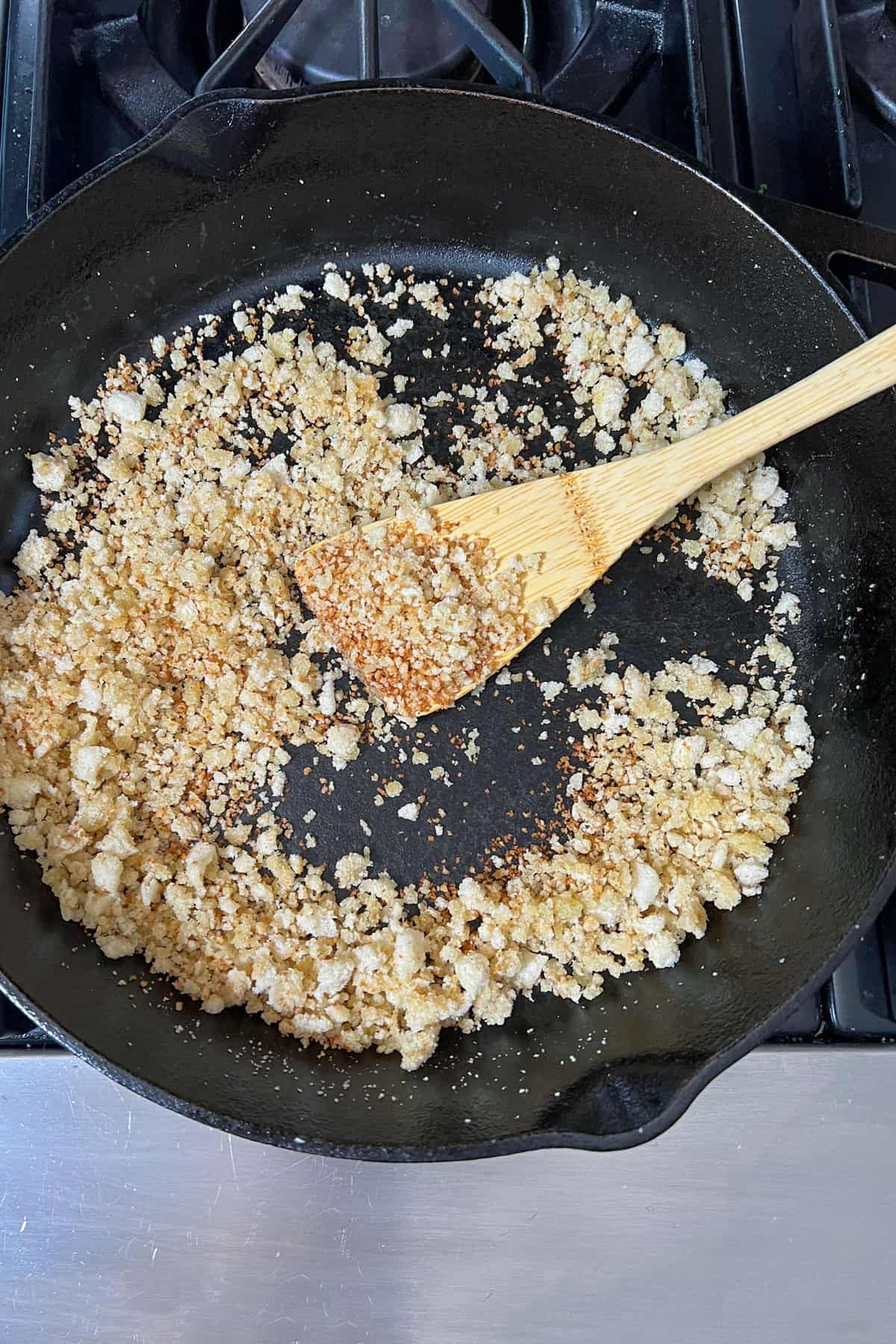 Breadcrumbs in a cast iron skillet with a wooden spatula