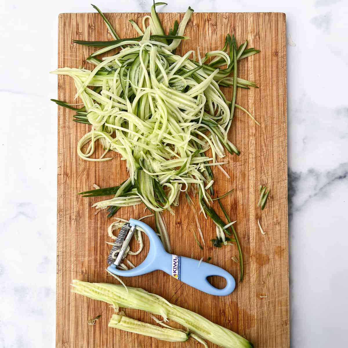 shredded cucumber on a wooden cutting board with a Thai vegetable peeler/shredder.