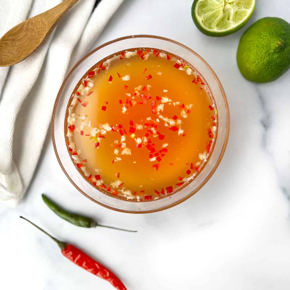 Vietnamese nước chấm sauce in a glass bowl with a couple of Thai chilis on the side and two halves of a squeezed lime.