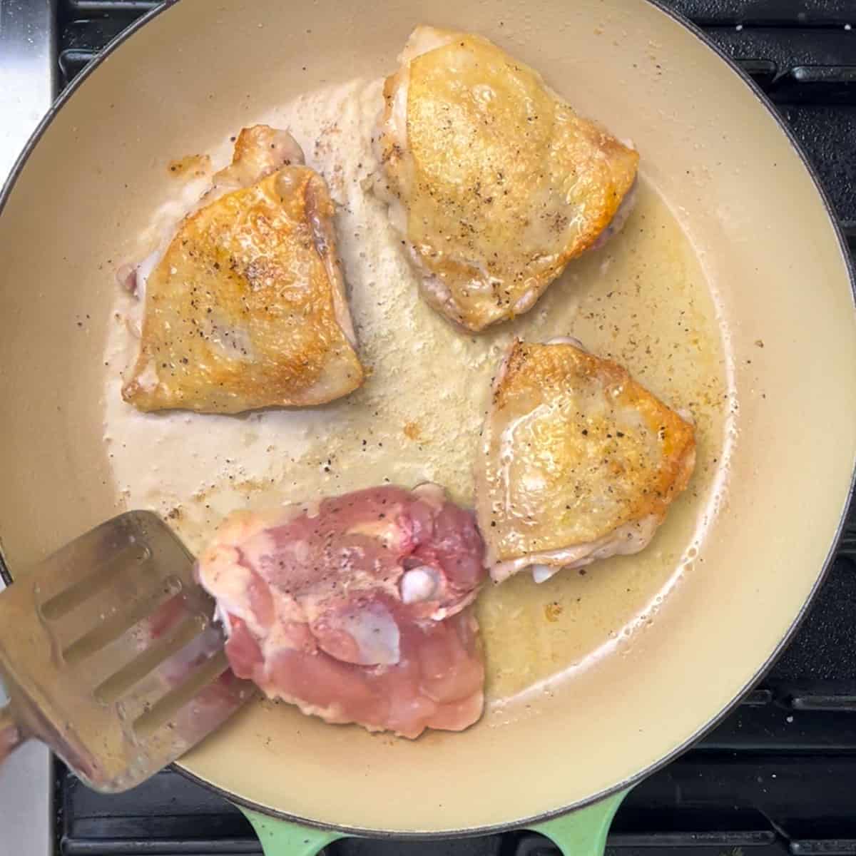 4 chicken thighs searing in a shallow dutch oven, three are skin side up.