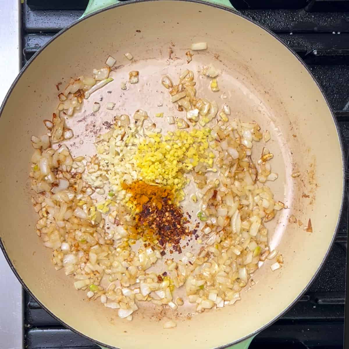 sautéd chopped onions in a shallow dutch oven with raw chopped ginger and garlic on top and some turmeric and red chili flakes.