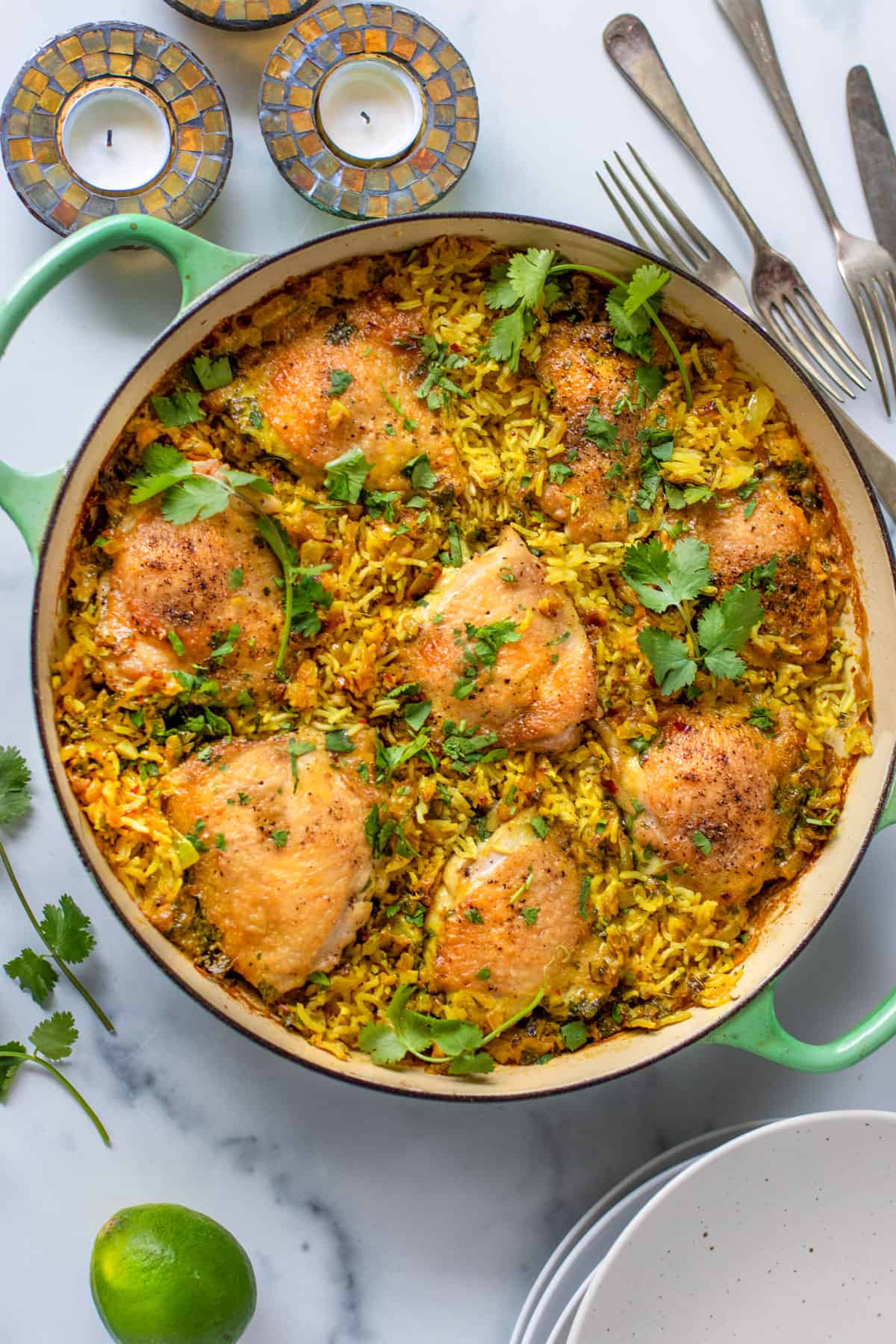 Chicken thighs and rice in a shallow green dutch oven, topped with chopped cilantro.