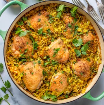 shallow round dutch oven filled with baked chicken thighs and rice topped with chopped cilantro.