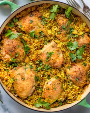 shallow round dutch oven filled with baked chicken thighs and rice topped with chopped cilantro.